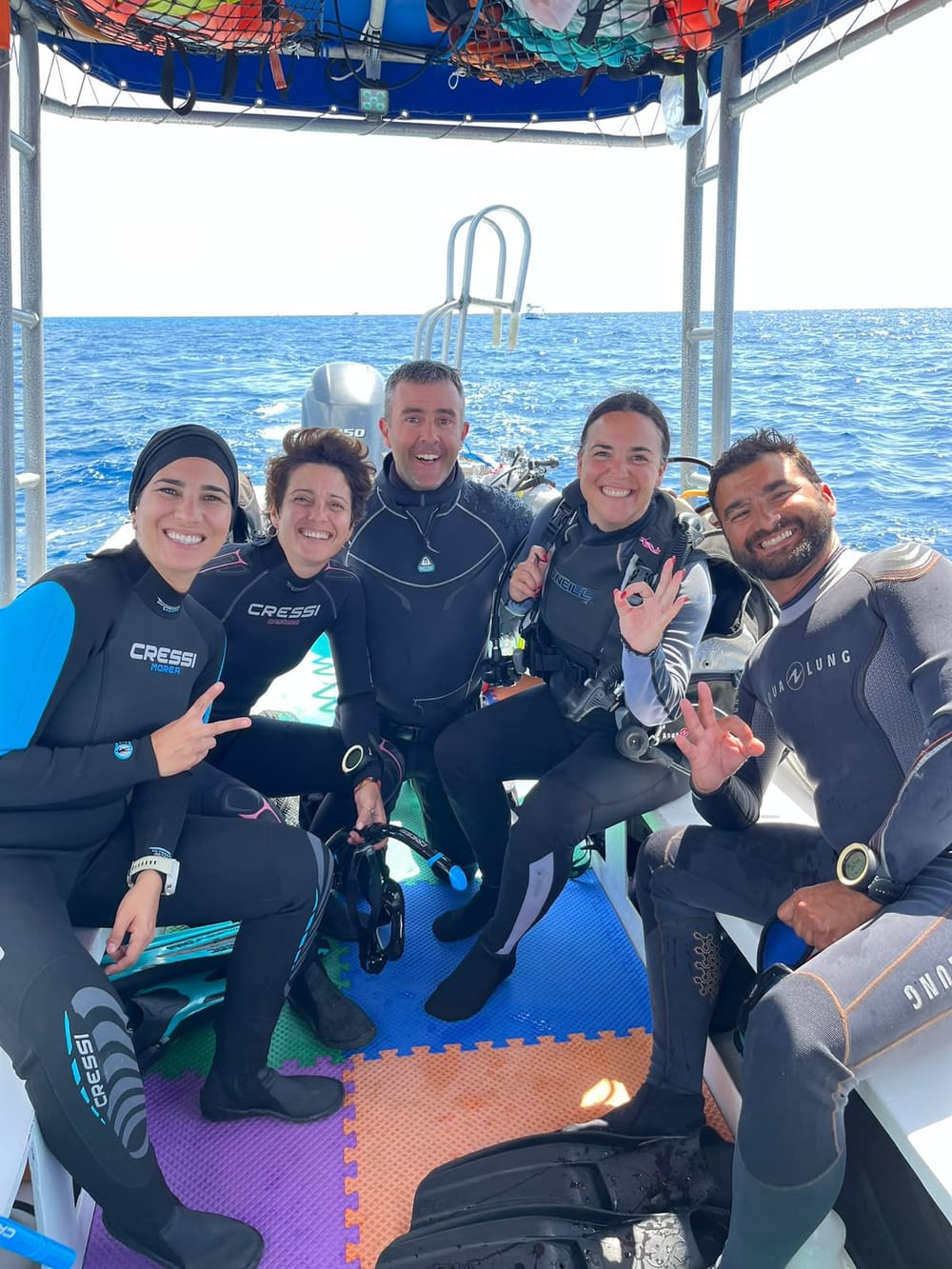 A group of divers with their guide on the boat, giving the OK sign